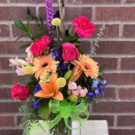 Mixed bouquet in a glass vase with bright pink, orange, purple, and blue flowers