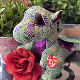 Plush dragon with a red rose and pink flowers in the background