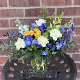 Mixed bouquet of blue, white, and yellow flowers in a glass vase