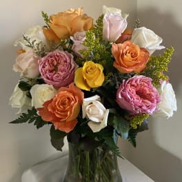 Mixed roses in orange, pink, yellow, and white in a glass vase