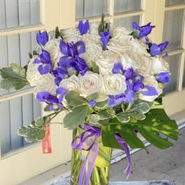 White roses and purple irises in a glass vase with a ribbon