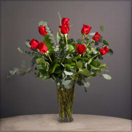 Red roses arranged in a clear glass vase with eucalyptus foliage