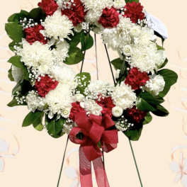 Red and white floral wreath with a red ribbon bow on a stand
