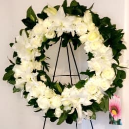 White floral wreath on a black stand with dark green leaves