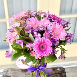 Pink and purple mixed bouquet in a glass vase with a purple ribbon