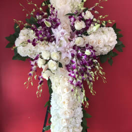 Large white floral cross with purple orchids on a stand