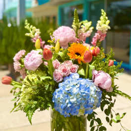 Mixed bouquet in a glass vase with blue hydrangea, pink roses, tulips, and orange gerbera daisies