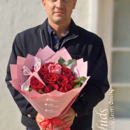 Man holding a bouquet of red roses wrapped in pink paper