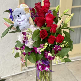 Red roses and purple orchids in a clear vase with a teddy bear