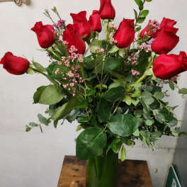 Bouquet of red roses with pink filler flowers in a green glass vase