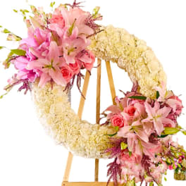 Floral wreath on an easel with pink lilies, roses, and cream flowers