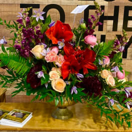 Large mixed floral arrangement in a gold vase with red, pink, and purple blooms