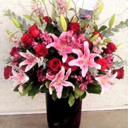 Pink lilies and red roses arranged in a dark vase