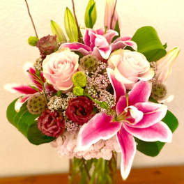 Pink lilies and roses arranged in a clear glass vase