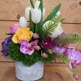 Colorful floral arrangement in a white decorative pot with tulips and orchids