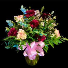 Bouquet of burgundy and blush carnations in a glass vase with a pink ribbon