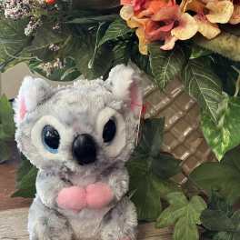 Plush koala toy in front of a floral arrangement with orange blooms