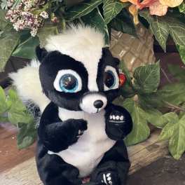 Plush skunk toy sitting in front of an artificial floral arrangement
