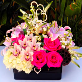 Pink roses and lilies arranged in a black box with heart picks