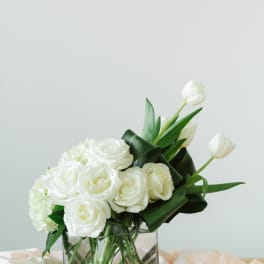 White roses and tulips arranged in a clear glass vase