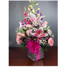 Pink and purple floral arrangement in a square glass vase with a butterfly accent