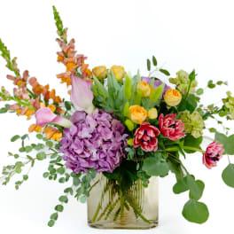 Mixed bouquet with purple hydrangea, yellow roses, and pink tulips in a glass vase
