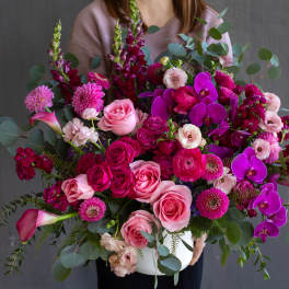 Large bouquet of pink roses, magenta blooms, and purple orchids in a white vase