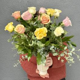 Person holding a bouquet of pastel roses in a ribbed vase