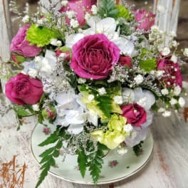 Compact pink rose and white hydrangea arrangement in a floral teacup on a rustic table