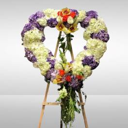 Heart-shaped floral wreath on an easel with purple, white, and red flowers