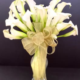 Bouquet of white calla lilies tied with a gold ribbon in a glass vase