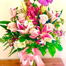 Pink roses and lilies in a glass vase with a pink ribbon and butterfly pick