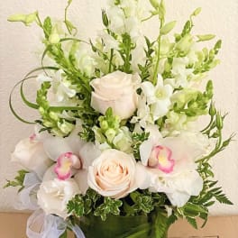 White and pale pink floral arrangement in a green vase with a ribbon