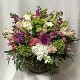 Lush low arrangement of pink roses, white hydrangeas, lilies and bright purple blooms in a clear glass bowl vase