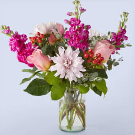 Pink roses, white mums, and bright magenta flowers in a clear glass vase