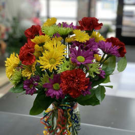 Colorful bouquet of daisies and carnations in a glass vase with ribbon curls