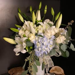 White lilies and pale blue hydrangeas in a white vase with ribbon