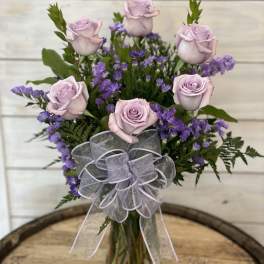 Lavender roses and purple filler flowers in a clear glass vase with a sheer bow