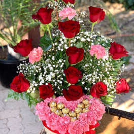 Basket arrangement of red roses, pink carnations, and chocolates