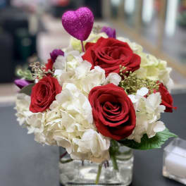 Red roses and white hydrangeas in a glass vase with a pink heart pick