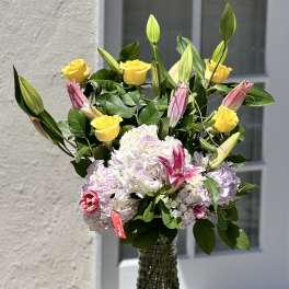 Bouquet of yellow roses, pink lilies, and pale hydrangeas in a glass vase
