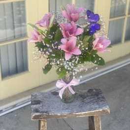 Pink lilies in a glass vase with a purple butterfly decoration
