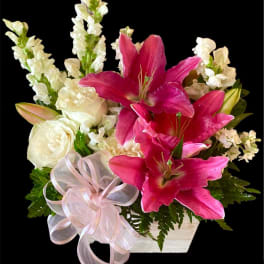 Pink lilies and white roses in a white container with a ribbon bow