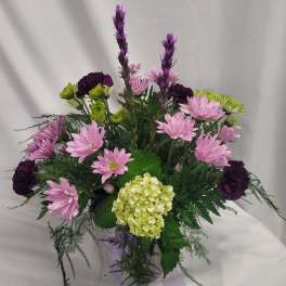Pink daisies and purple carnations in a clear vase with a hydrangea bloom