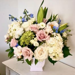 Bouquet of pastel roses, hydrangeas, lilies, and blue flowers in a white vase