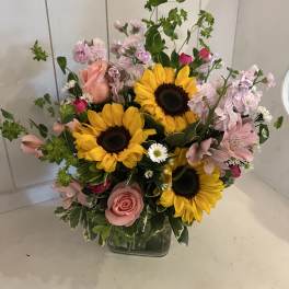 Mixed bouquet with sunflowers, pink roses, and pale pink blooms in a glass vase