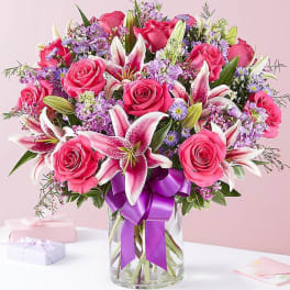 Pink roses and lilies in a glass vase with a purple ribbon