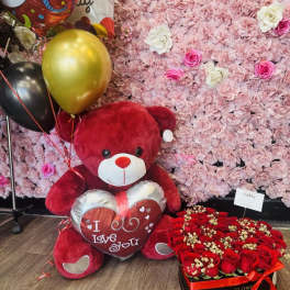 Red teddy bear with balloons beside a heart-shaped box of red roses