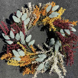 Circular wreath of colorful dried flowers on dark pavement