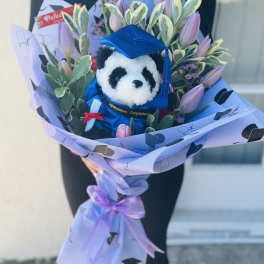 Bouquet with a plush panda in a blue graduation cap surrounded by pink tulips